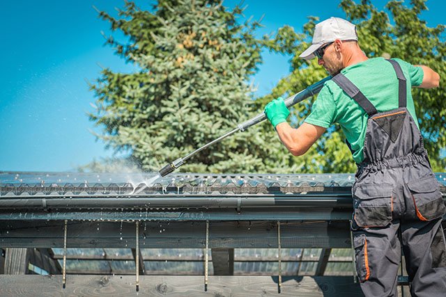 Man pressure washing a home's gutters and roof